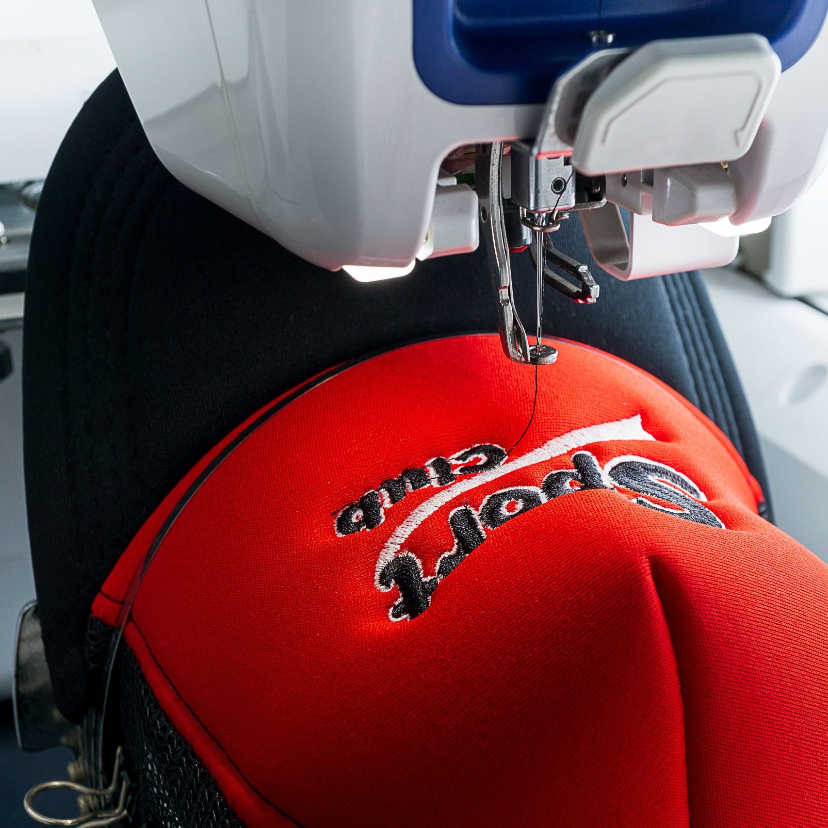 White Embroidery machine and red and black sport cap on the hoop, close up picture